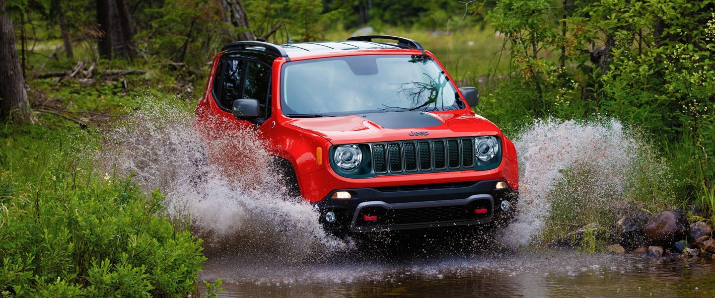 The 2021 Jeep Renegade being driven through a stream with water splashing on both sides of the vehicle.