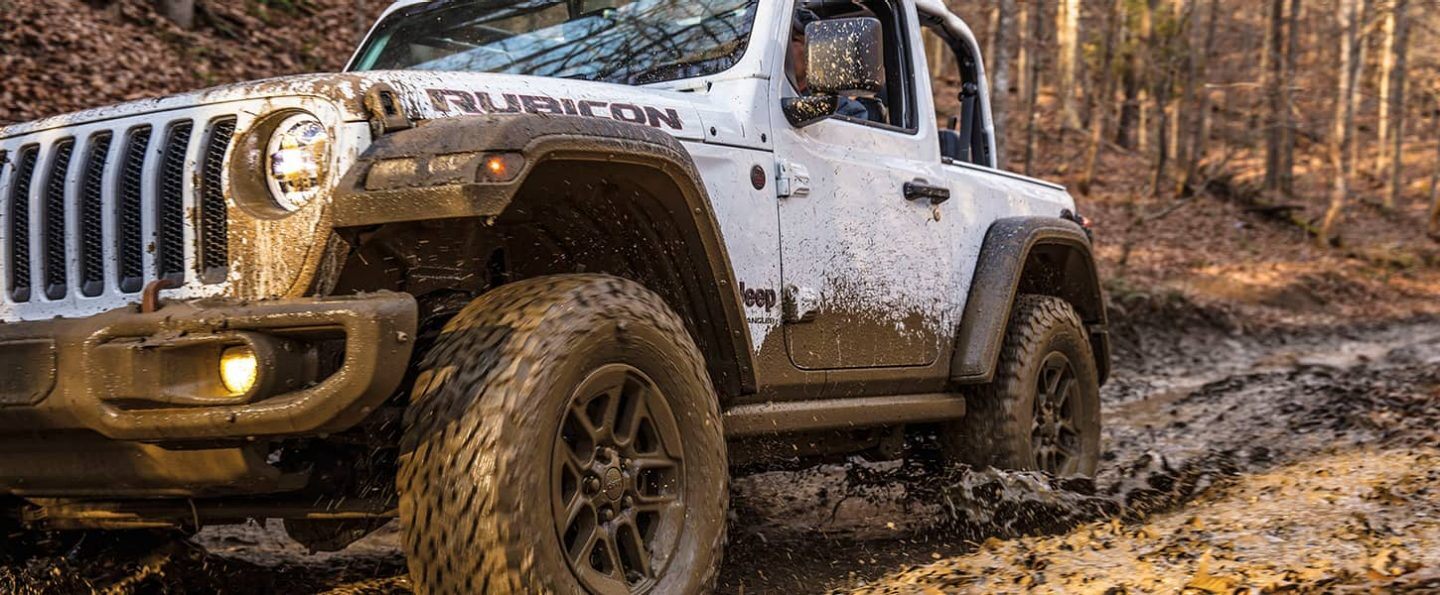 A mud-spattered 2021 Jeep Wrangler Rubicon being driven on a trail.
