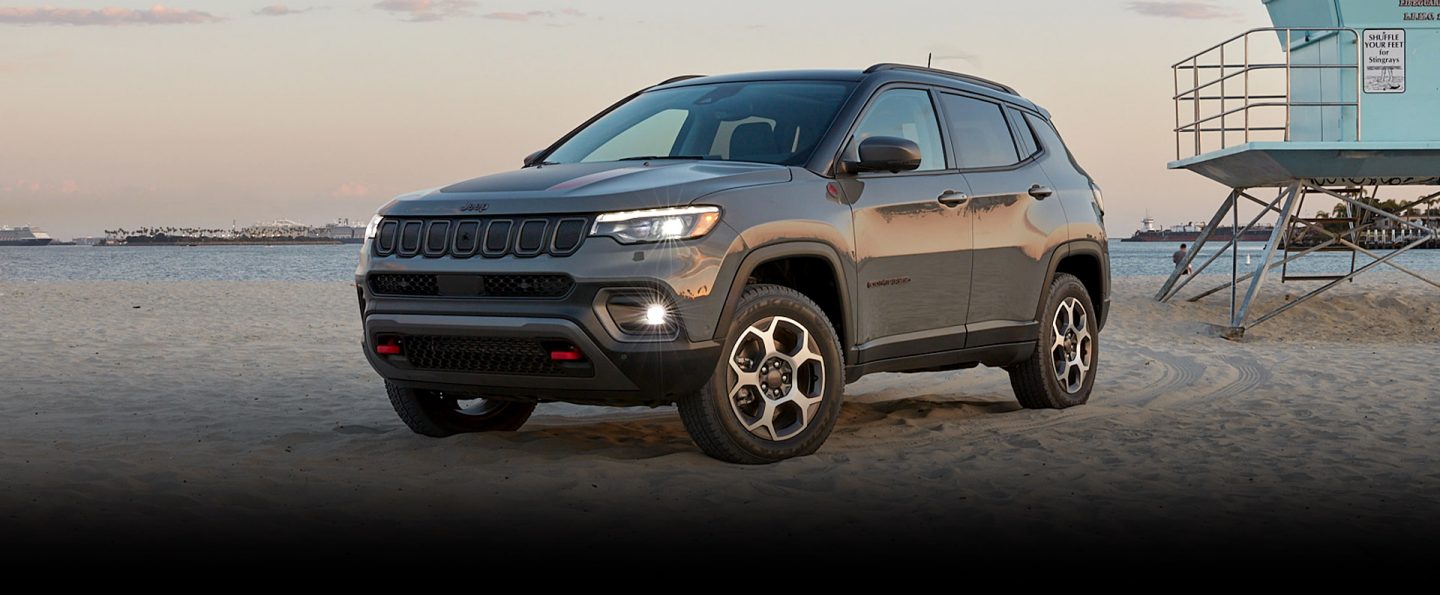 The Jeep Compass Trailhawk parked on a beach with tire tracks visible on the sand behind it.