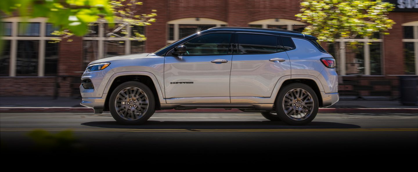 The Jeep Compass High Altitude being driven down a street past a row of brick buildings.
